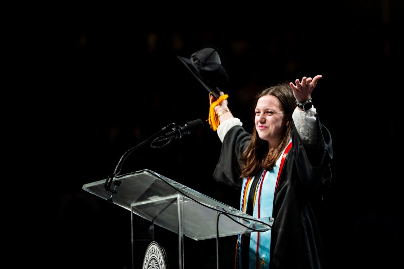 Speaker at the College of Science graduation ceremony holding their cap in the air. 