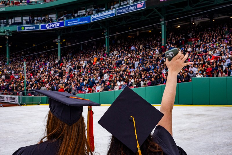 Two graduates in regalia look out to a stadium full of celebrants