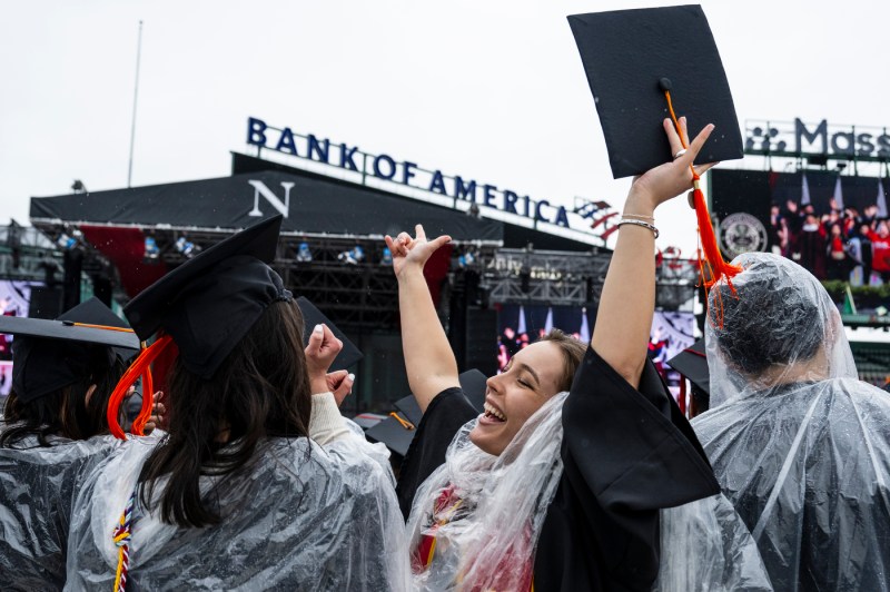 Graduates wearing ponchos cheering with their arms raised.
