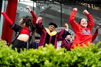 People wearing regalia dance together at a graduation ceremony.