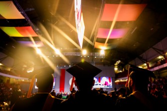 People wearing regalia attend commencement in a large arena.