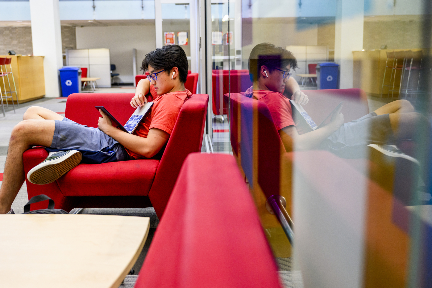 A person reads inside a library while sitting on a red chair. 