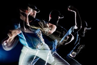 A stylized time lapse photo of a baseball player running in front of a dark studio background.