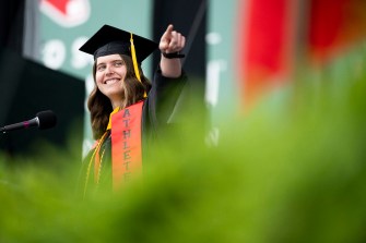 Headshot of Megan Carter in graduation regalia smiling and pointing off camera