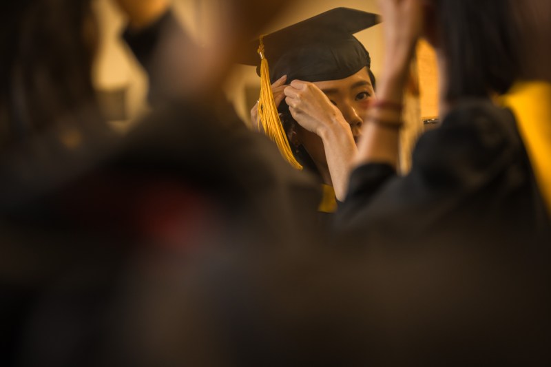 A person adjusts their regalia in front of a mirror.