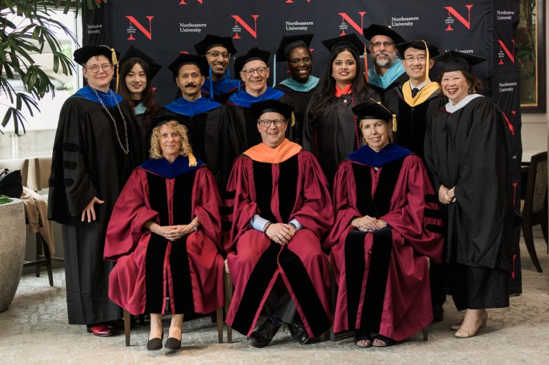 Thirteen people wearing regalia take a picture at Seattle's Commencement ceremony.