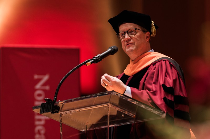 A person wearing regalia speaks at a podium. 