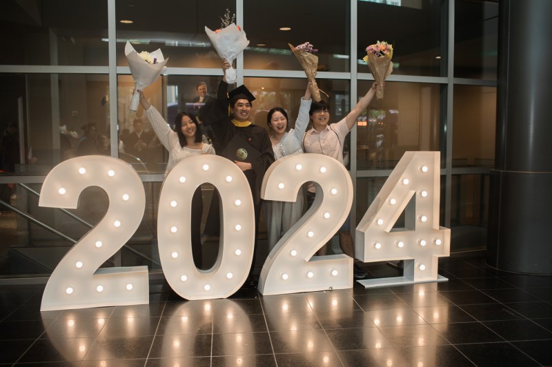Four people stand in front of a display of large, brightly lit numbers: "2024".