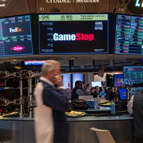 Traders walking on the floor at the New York Stock Exchange in front of a screen displaying the GameStop logo.