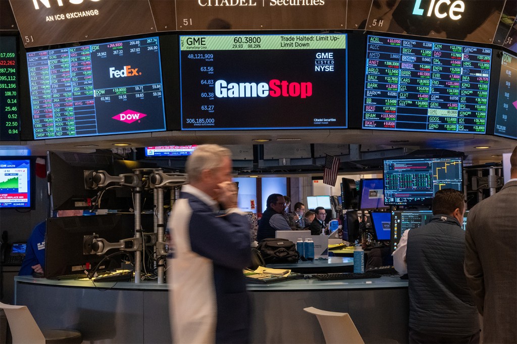 Traders walking on the floor at the New York Stock Exchange in front of a screen displaying the GameStop logo.