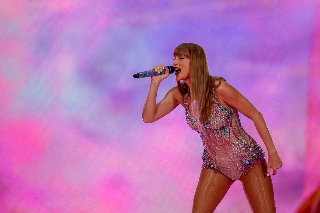 Taylor Swift wearing a glittering bodysuit singing during a performance of the Eras Tour.