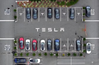 Tesla cars sitting in a parking lot branded with the Tesla logo.