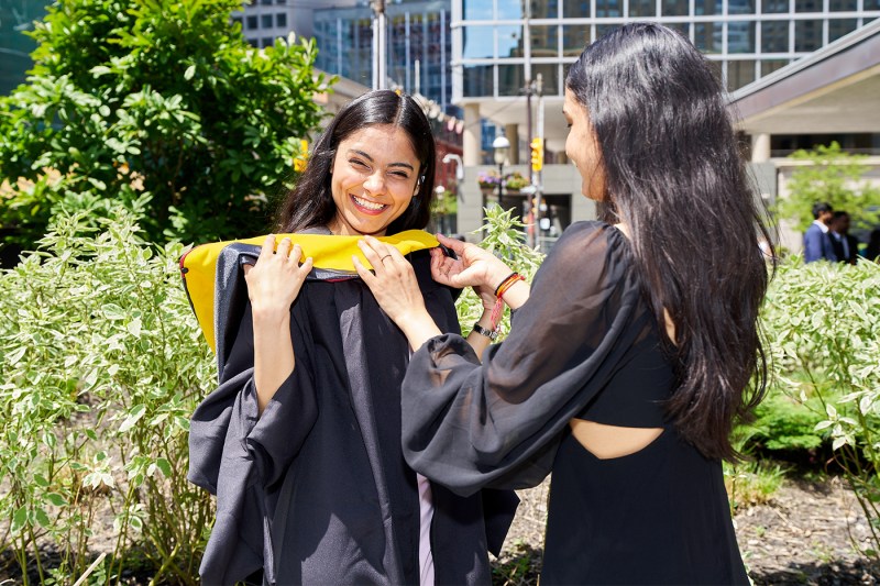 A student helps another adjust their hood.