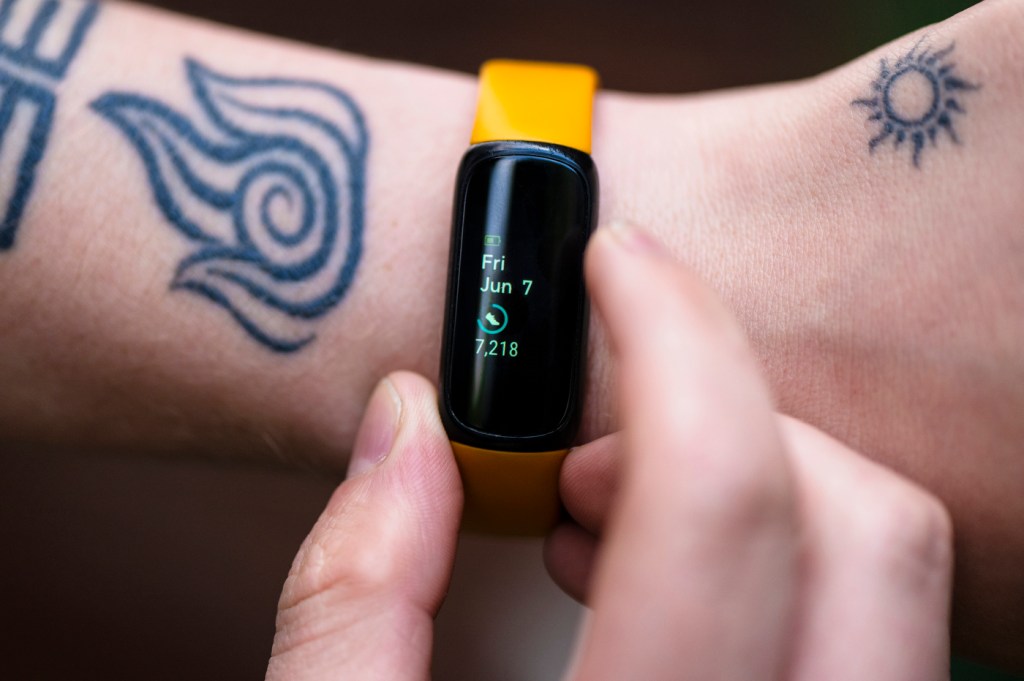 A hand checking a smart watch, which displays 7,218 steps.