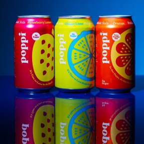 Three cans of Poppi soda on a blue background.