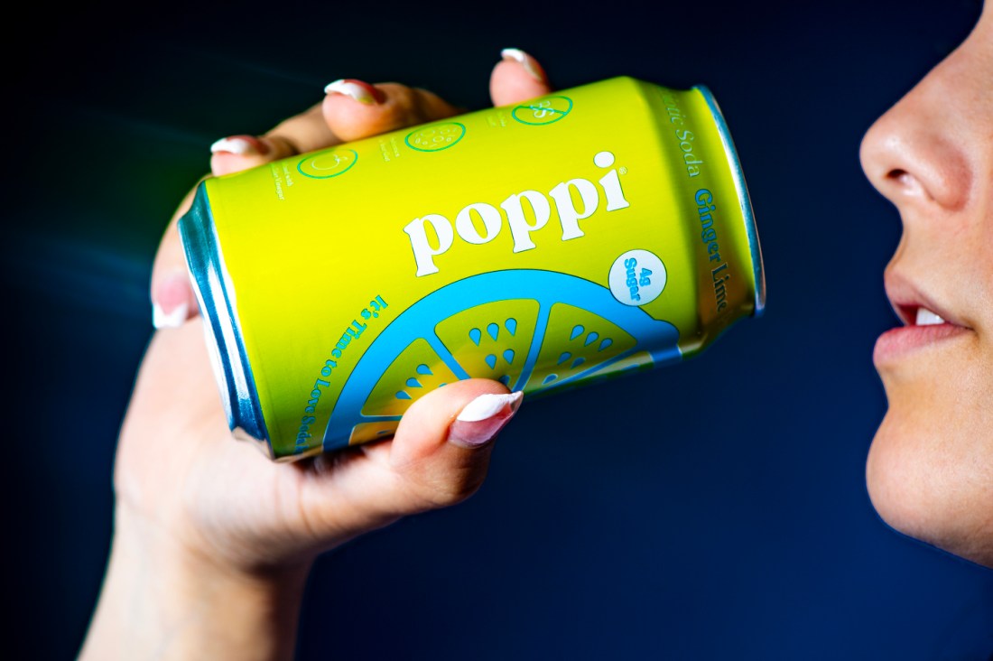 Person tilts back lime green can of Poppi.