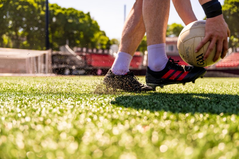 A gaelic football player holding the ball right above their cleats.