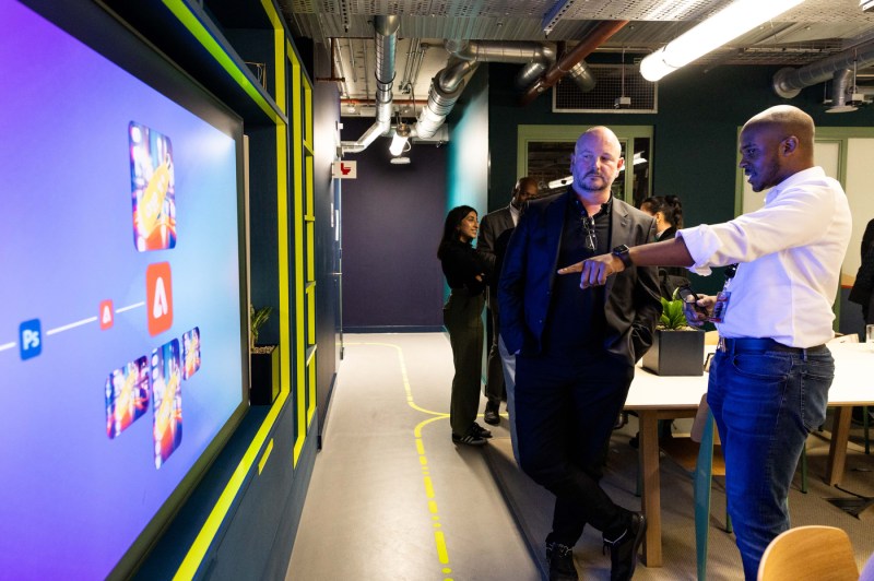 Two people standing in front of a screen at the Adobe offices, one pointing to what is on the screen.