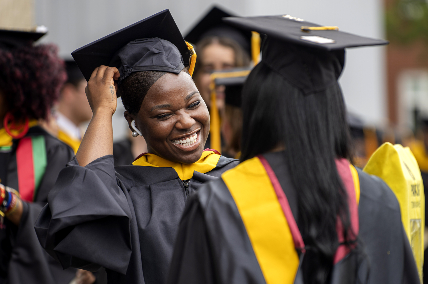 Two graduates smiling and adjusting their caps at the Roux Institute commencement ceremony.