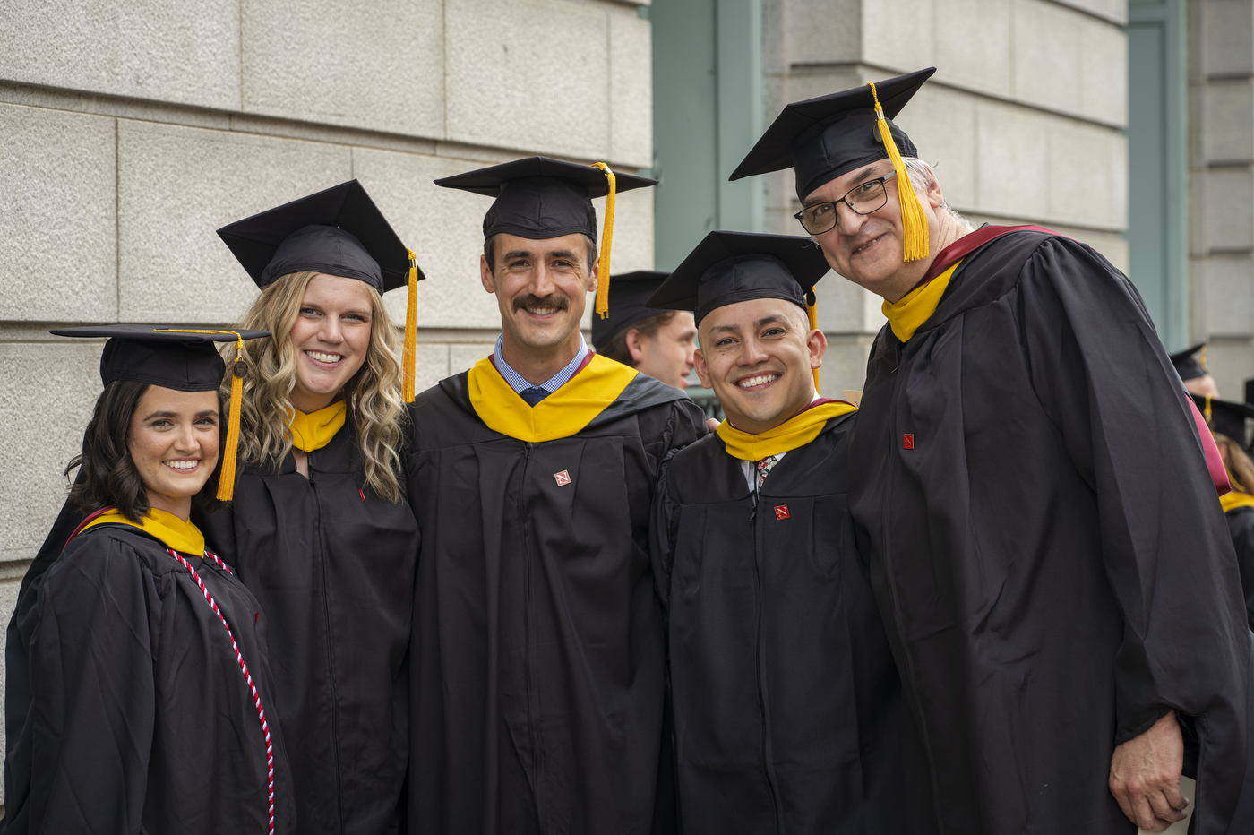 Five graduates posing together in their caps and gowns.