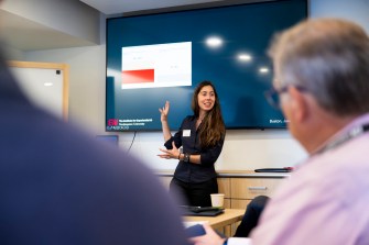 Cansu Cana speaks in a conference room in front of a blue screen.