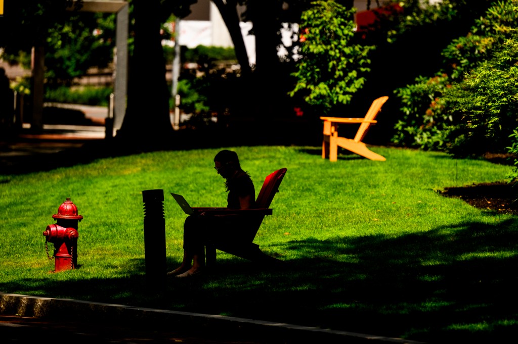 A person works on their laptop while sitting on a lawn chair outside.