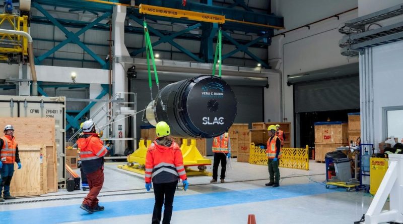 People in a warehouse looking at The Rubin Observatory Legacy Survey of Space and Time camera.