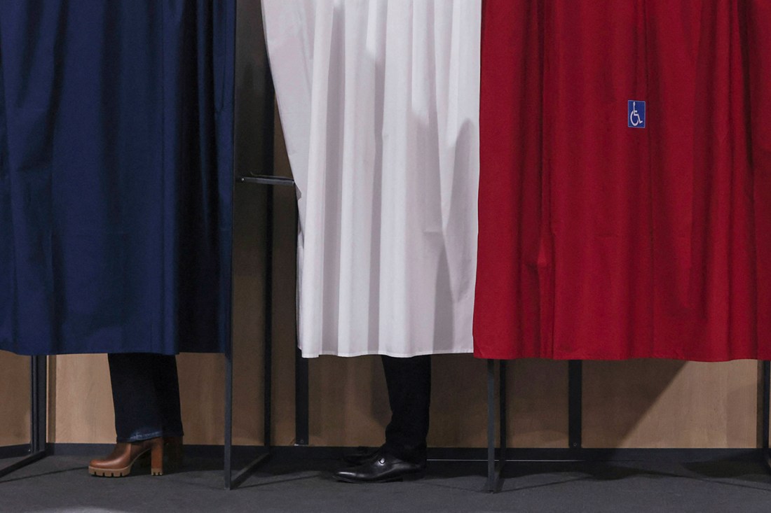 People's feet hidden behind blue, white, and red cloths at a voting station.