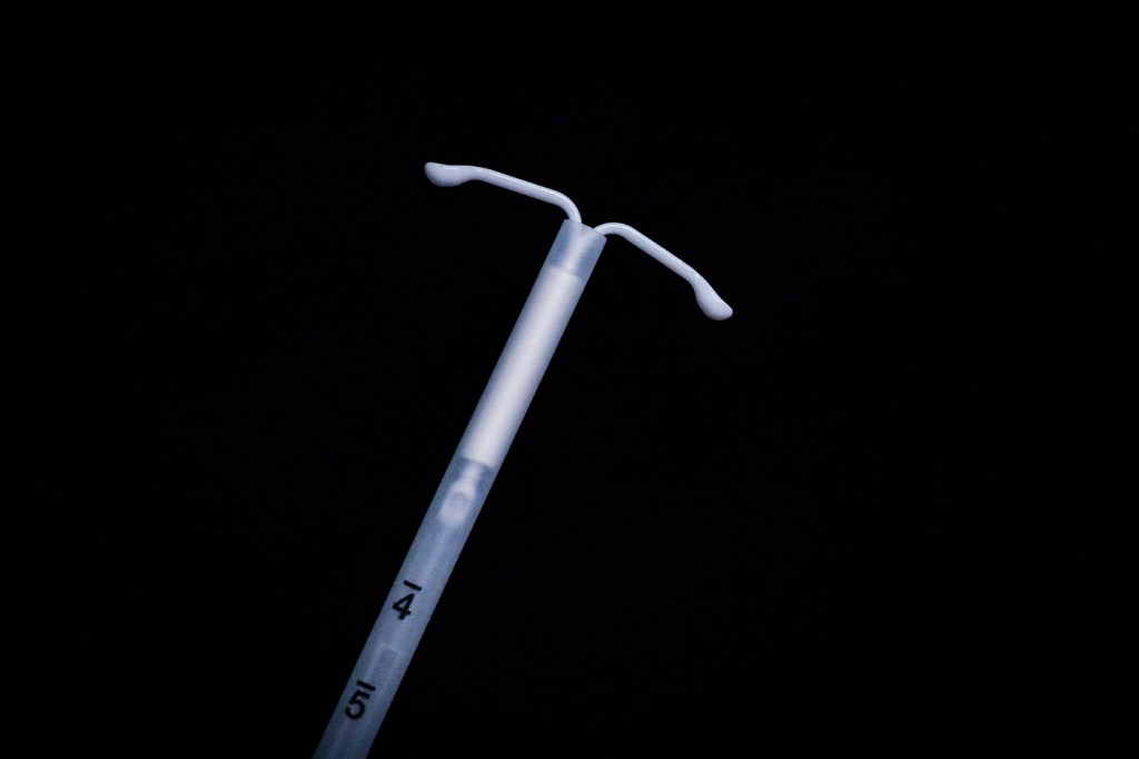 A hormonal IUD hovers over a black background.