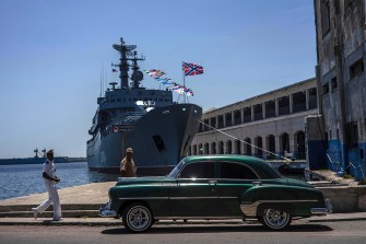 A Cuban sailor walking outside in the sun past a Russian Navy ship.