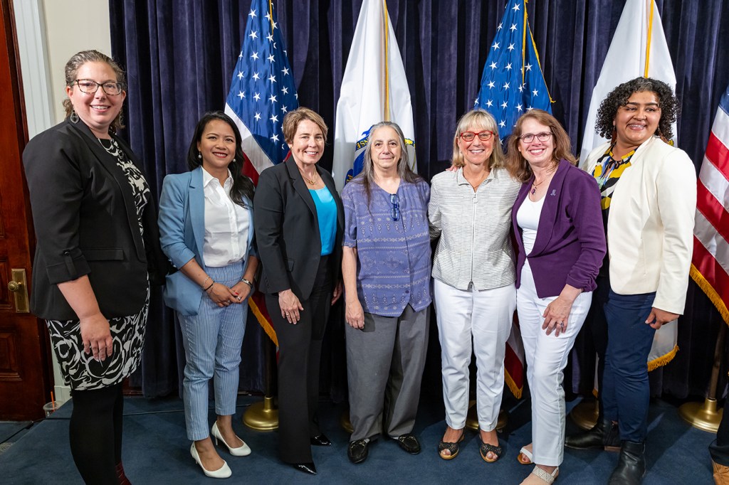 Multiple people pose in front of flags for a photo.