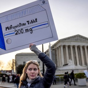 A protestor holding a sign that depicts a drawing of a box of Mifepristone pills.