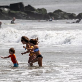 Three people play in the ocean at the beach on a sunny day.