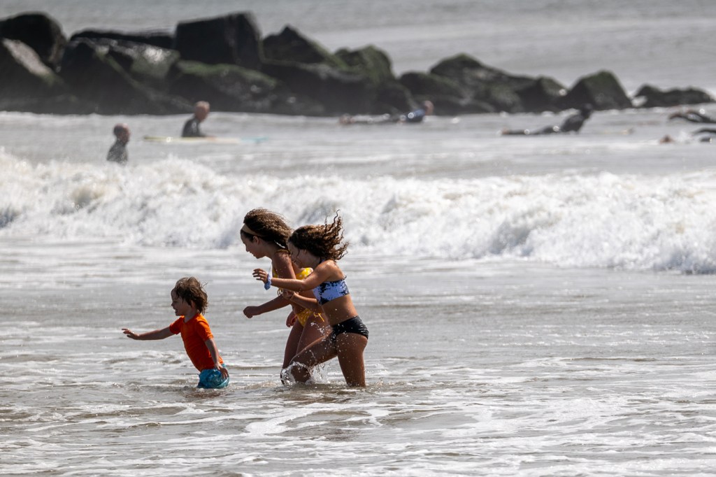 Three people play in the ocean at the beach on a sunny day.