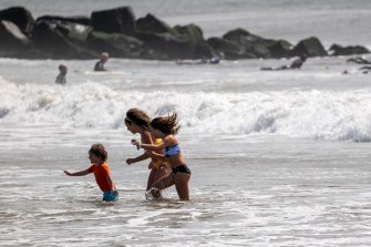 Three people play in the ocean at the beach on a sunny day.