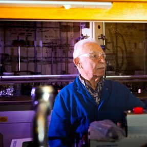 Alexandros Makriyannis, director of the Center for Drug Discovery at Northeastern University, poses for a portrait holding up a flask of purple liquid.