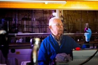 Alexandros Makriyannis, director of the Center for Drug Discovery at Northeastern University, poses for a portrait holding up a flask of purple liquid.