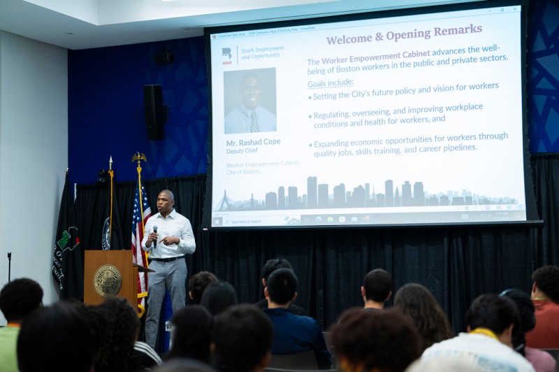 Rashad Cope, Deputy Chief of the City’s Worker Empowerment Cabinet, stands on stage, giving the welcome and opening remarks to a crowd of listening students.