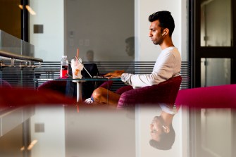 A Northeastern graduate sits at a table on campus and does work on a computer.