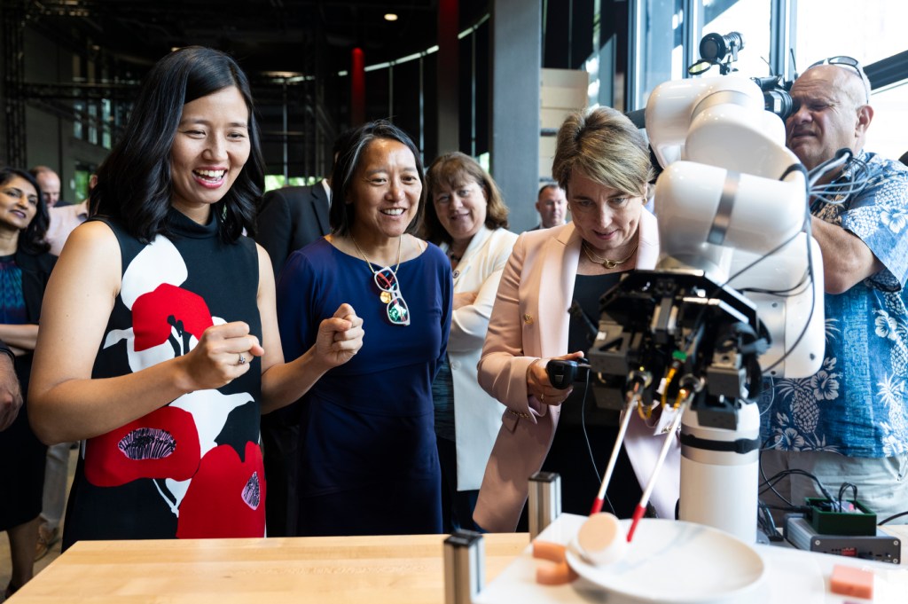 Gov. Healey, Boston Mayor Wu, and other state leaders look on as a robot performs a function on a table.