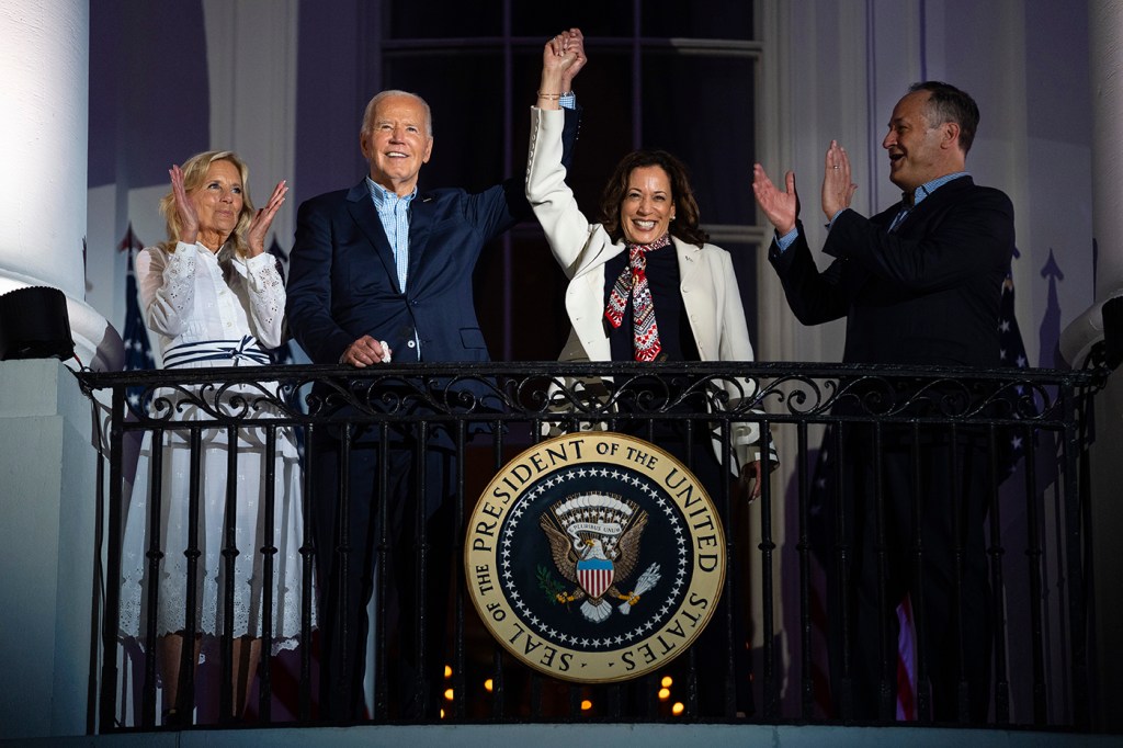 Joe Biden and Kamala Harris stand on a balcony raising their hands together.