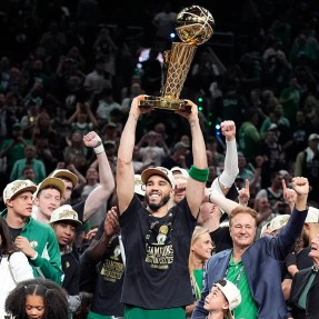 Jayson Tatum holding up a championship trophy while surrounded by other members of the Boston Celtics team.