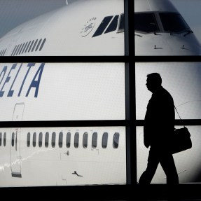 The silhouette of a person holding a briefcase walks in front of a grounded plane.