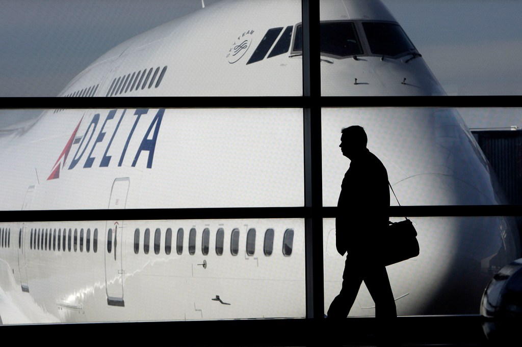 The silhouette of a person holding a briefcase walks in front of a grounded plane.