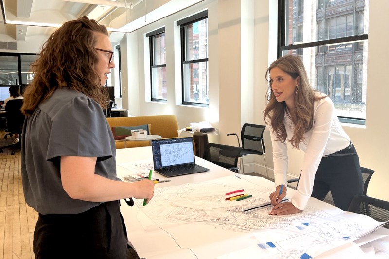 Kaitlin McCarthy leaning over a building plan on a table while speaking to someone standing on the other side of the table. 