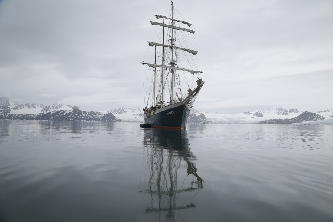 A tall ship in the water on a foggy day, with snowy mountains in the background.