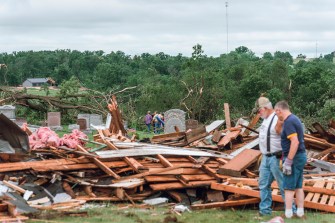 People looking at the rubble of a house from a tornado's destruction.