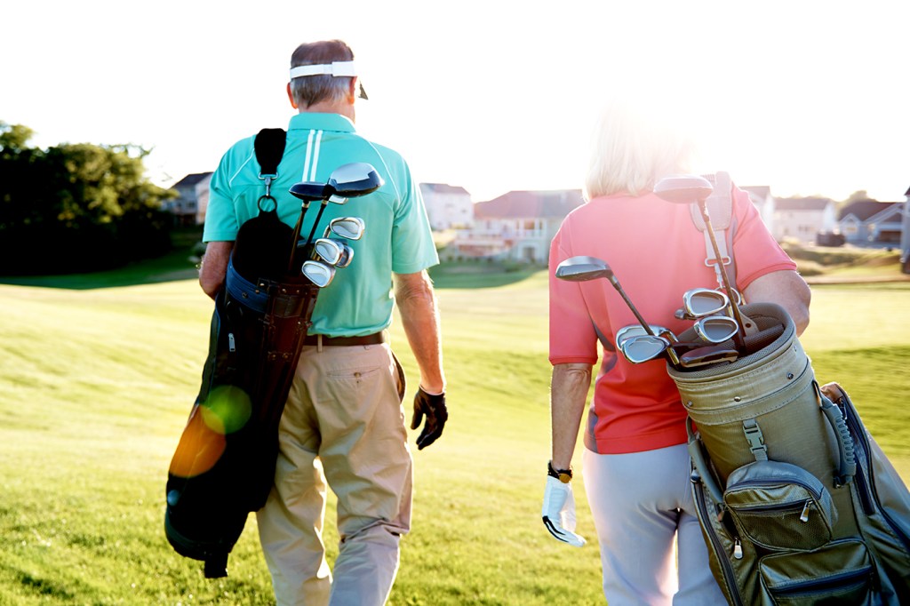 Two people walk together across a golf course while carrying their golf bags.