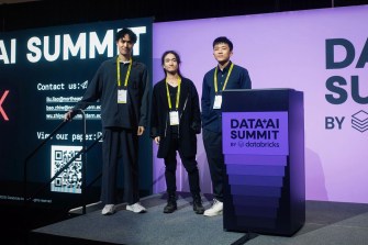 Three students stand on a stage in front of a purple backdrop.