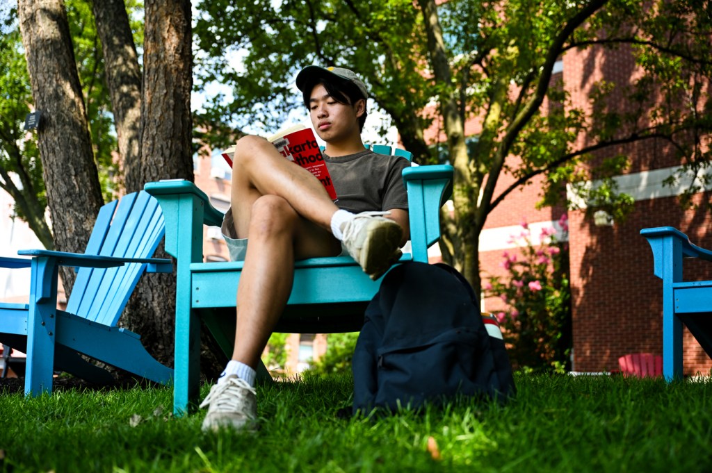 A person reading a book sits in a bright blue lawn chair outside on a sunny day.